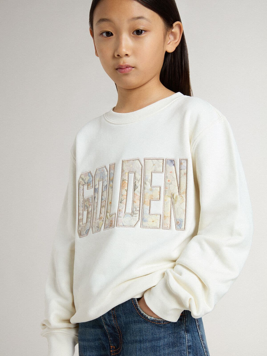 witte meisjestrui met veelkleurige gouden letters op de voorkant.