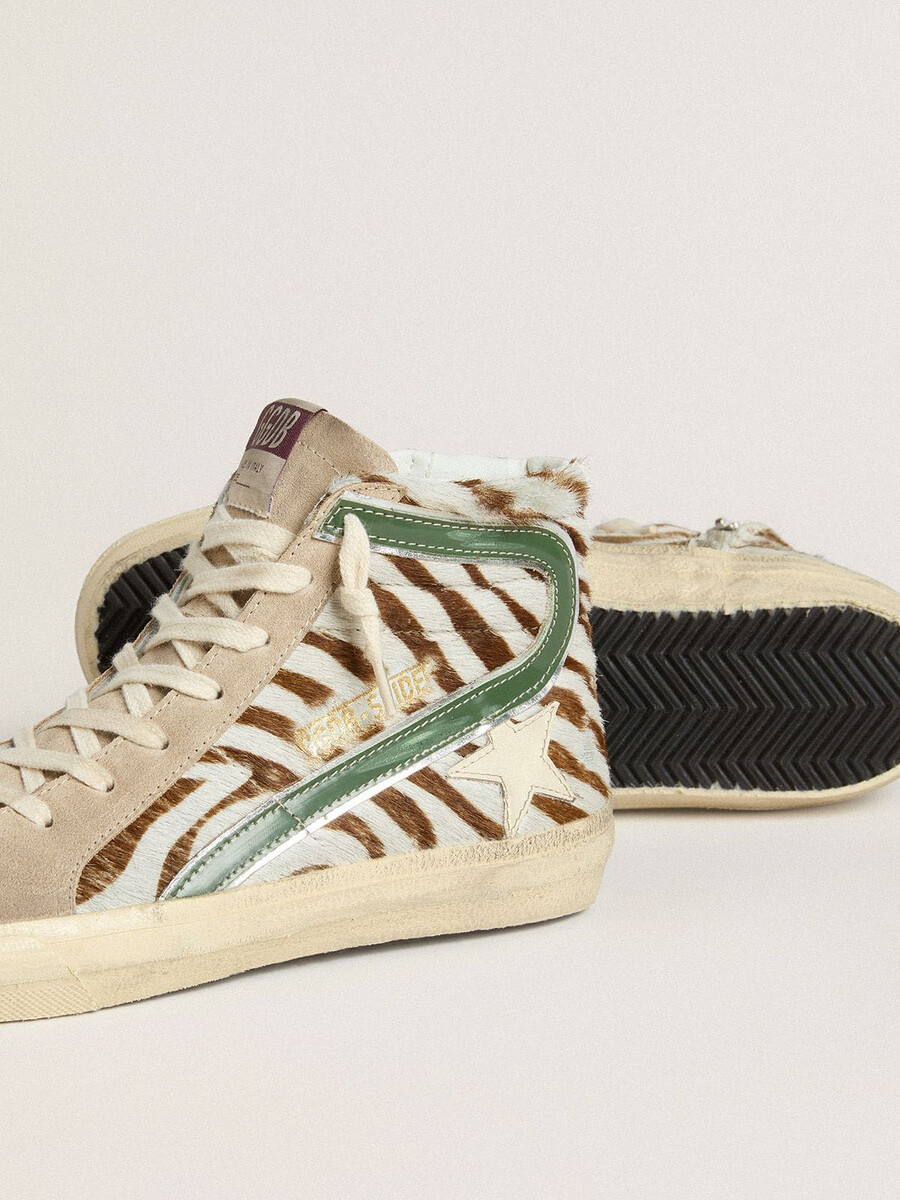damesslippers van ponyhuid met zebraprint en groene gelamineerde leren accenten.