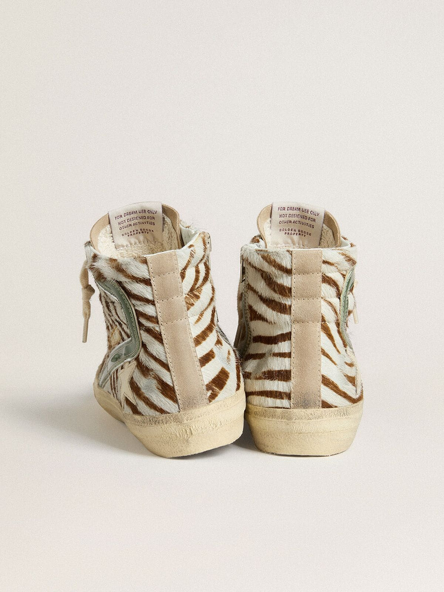 damesslippers van ponyhuid met zebraprint en groene gelamineerde leren accenten.