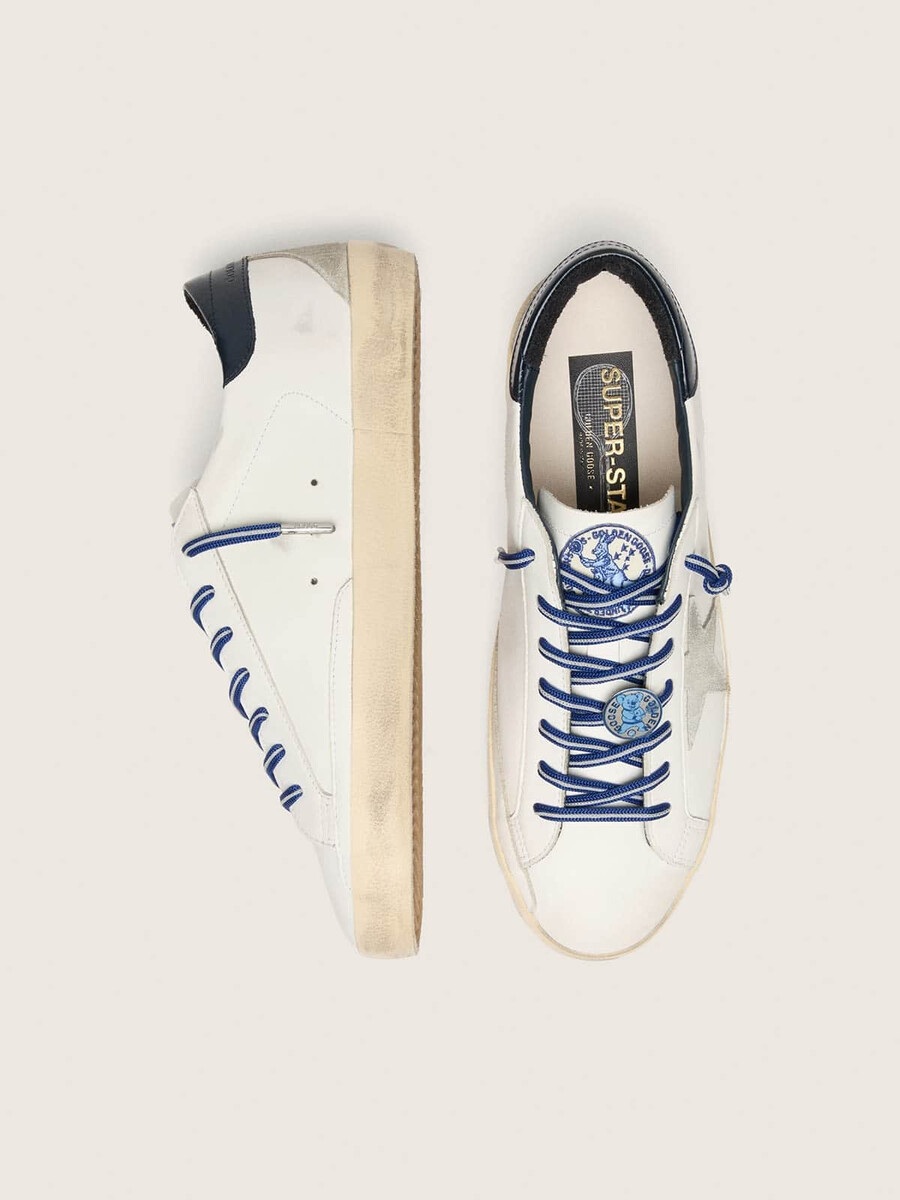 de super-star ltd herensneaker geïnspireerd op tennis is uitgevoerd in wit leer met een suède ster en een blauwe leren hielband.