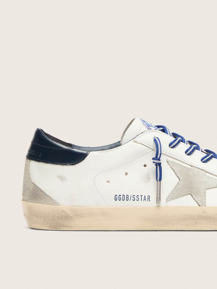 de super-star ltd herensneaker geïnspireerd op tennis is uitgevoerd in wit leer met een suède ster en een blauwe leren hielband.